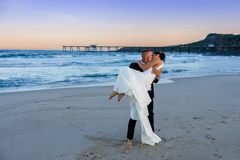 groom lifting bride on catherine hill bay beach